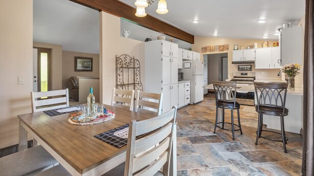 A spacious kitchen with white cabinets, a wooden dining table, and a bar area with stools. - Serene Riverside Retreat 3 Bedroom Home by RedAwning (Little Suamico)