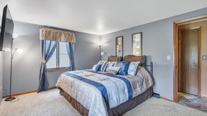 A bedroom with a large bed, a TV, a window with curtains, and a door. - Serene Riverside Retreat 3 Bedroom Home by RedAwning (Little Suamico)