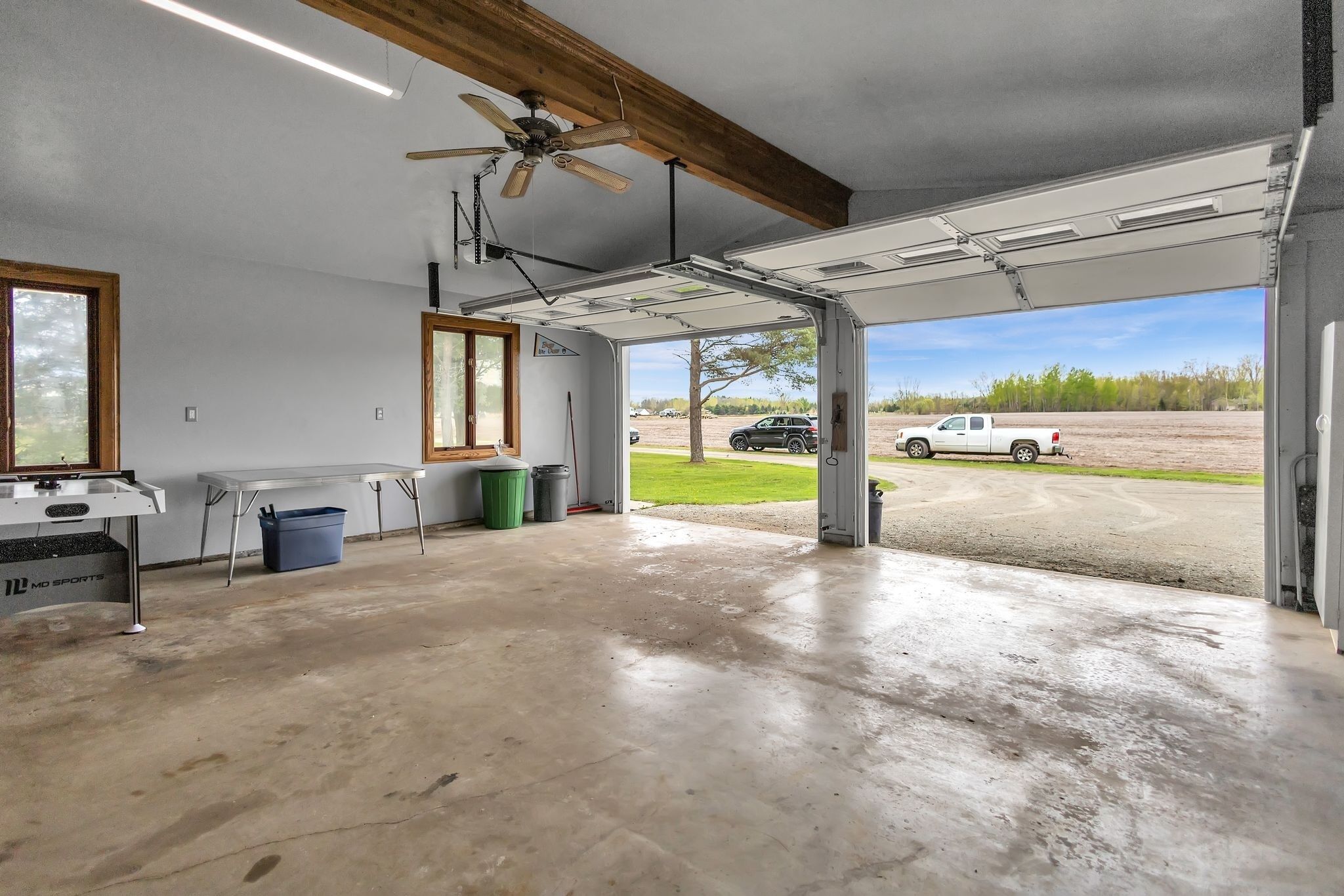 A garage with a concrete floor, a ceiling fan, and a table with a trash bin.
