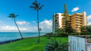 A beachfront hotel with a grassy lawn, palm trees, and a view of the ocean. - Royal Kahana 1211 2 Bedroom Condo (Lahaina)