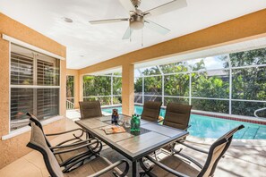 A covered outdoor dining area with a pool view, a ceiling fan, and a table set for four.