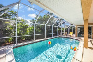 A swimming pool with a glass enclosure, surrounded by lush greenery and a clear blue sky.