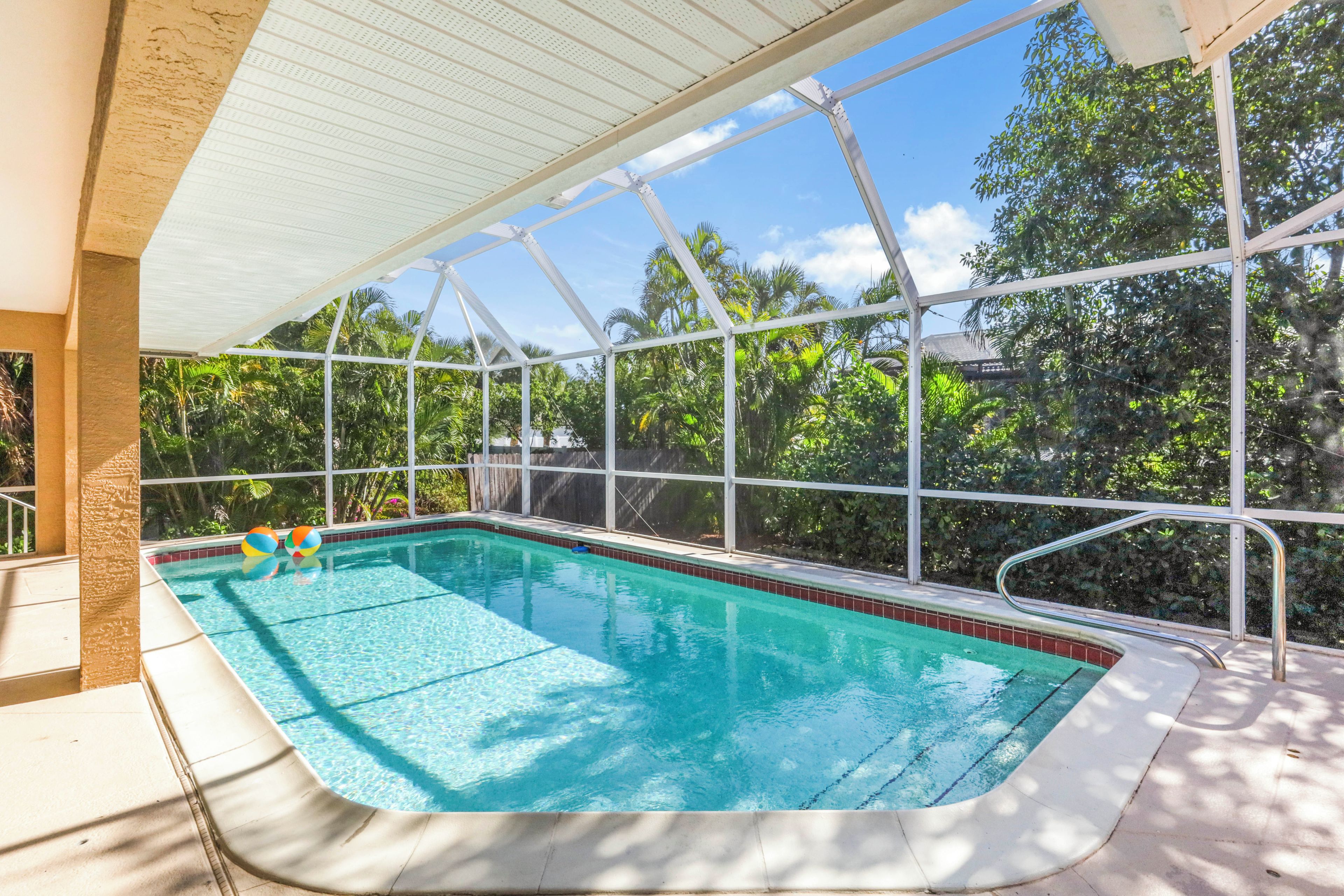 An indoor swimming pool with clear blue water, surrounded by a glass enclosure, and a view of lush greenery outside.