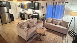 A spacious living area with two sofas, a coffee table, and a kitchen in the background. - Charming West Harwich Cottage, Newly Renovated, cozy but convenient location (Harwich)
