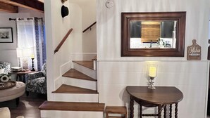A wooden staircase leading to a second floor, a dining table with a candle, and a kitchen area with a mirror and a sign. - Charming West Harwich Cottage, Newly Renovated, cozy but convenient location (Harwich)