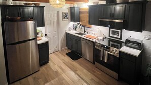 A modern kitchen with dark cabinets, stainless steel appliances, and a wooden ceiling. - Charming West Harwich Cottage, Newly Renovated, cozy but convenient location (Harwich)