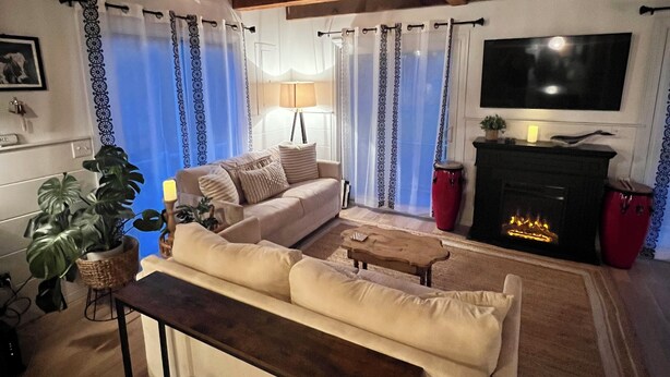 A cozy living room with a sofa, a coffee table, a fireplace, and a television mounted on the wall. - Charming West Harwich Cottage, Newly Renovated, cozy but convenient location (Harwich)