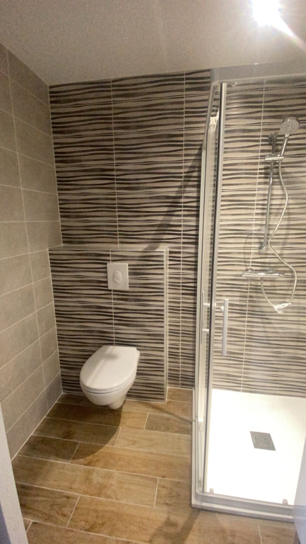 A bathroom with a toilet, a shower with a glass door, and striped wall tiles.