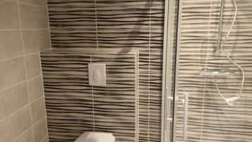 A bathroom with a toilet, a shower with a glass door, and striped wall tiles.