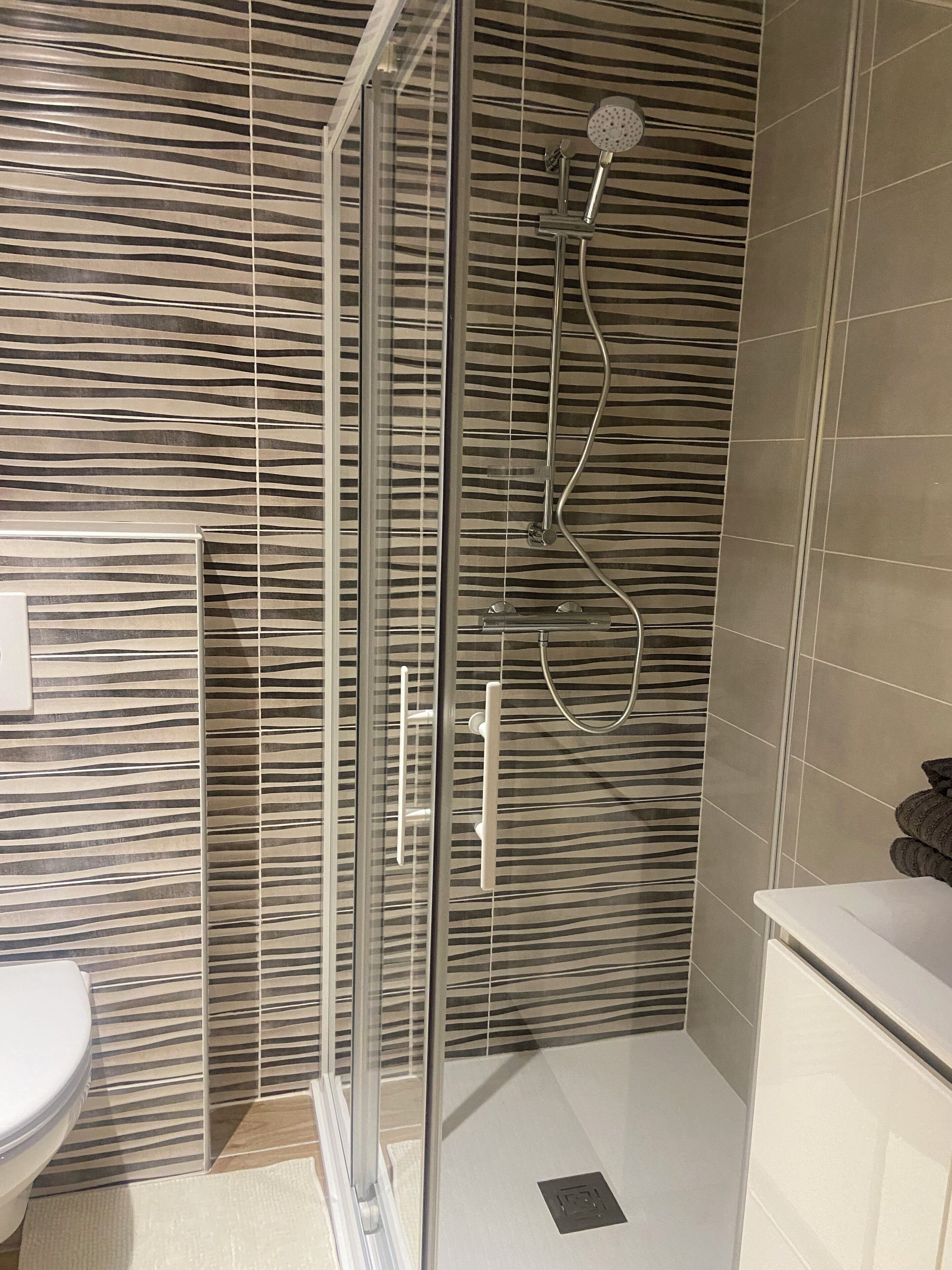A bathroom with a glass shower enclosure, a toilet, and a sink.