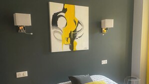 Hotellihuone, jossa on sänky, taulu seinällä ja kaksi seinään kiinnitettyä lamppua.