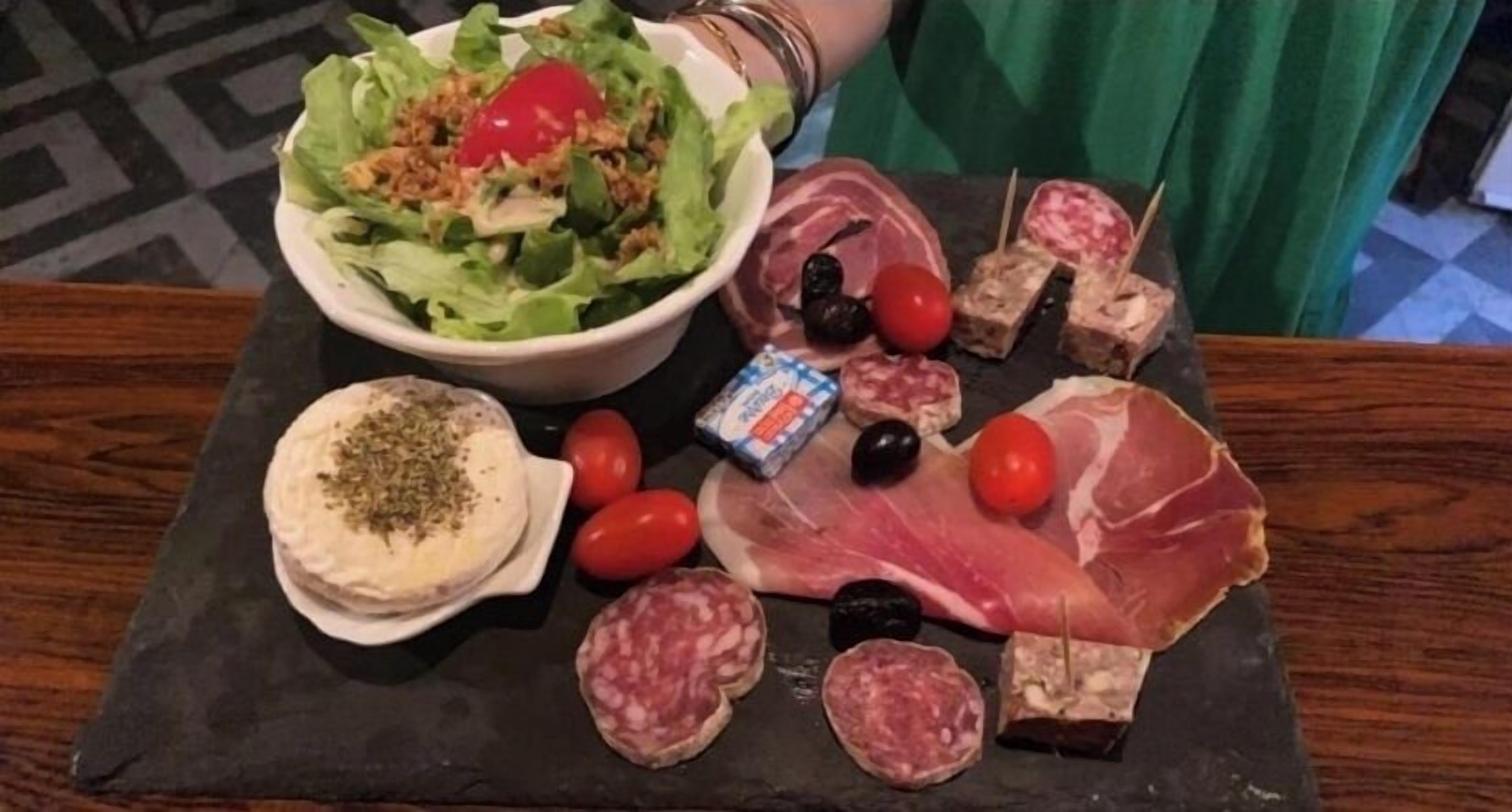 A variety of food items including a salad, meats, cheeses, and olives on a slate board.