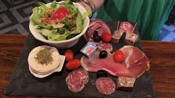 A variety of food items including a salad, meats, cheeses, and olives on a slate board.