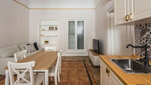 A compact kitchen with a dining area, white cabinetry, a tiled backsplash, and a small television. - Casa Core a Noto by Wonderful Italy (Noto)