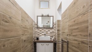 A bathroom with wooden walls, a tiled backsplash, a white sink, and a mirror above it. - Casa Core a Noto by Wonderful Italy (Noto)