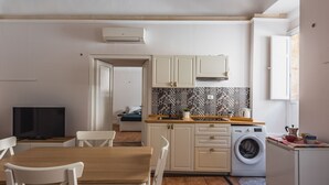 A compact kitchen with a washing machine, a dining area with a table and chairs, and a television. - Casa Core a Noto by Wonderful Italy (Noto)