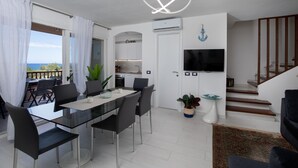A modern living room with a dining area, a staircase, and a view of the sea.