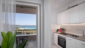 A modern kitchen with white cabinets, a stainless steel sink, and a view of the ocean through a balcony.