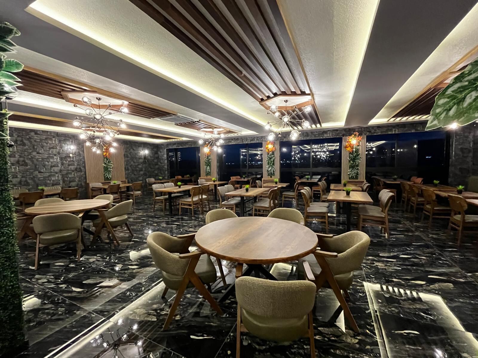 A restaurant with round tables and chairs, stone walls, and large windows.