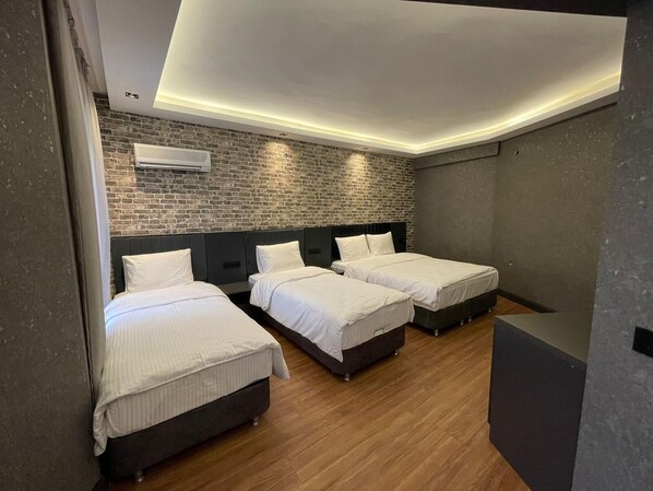 A modern hotel room with three beds, a brick wall, and a recessed ceiling light.