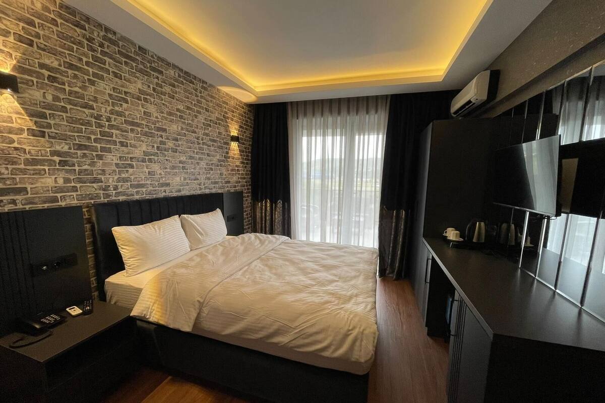 A modern hotel room with a brick wall, a large bed, a flat-screen TV, and a wooden floor.
