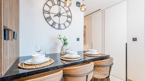 Une cuisine moderne avec un plan de travail en marbre noir, une grande horloge murale et un coin repas comprenant quatre chaises.