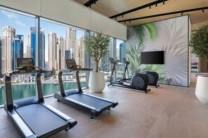 Ett modernt gym med löpband, motionscyklar och ett stort fönster med utsikt över staden.