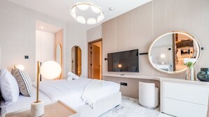 Une chambre d’hôtel moderne équipée d’un lit, d’une table de chevet, d’une lampe, d’un miroir, d’une télévision et d’une petite plante.