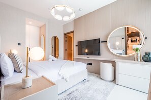 Moderni hotellihuone, jossa on sänky, yöpöytä, lamppu, peili, televisio ja pieni kasvi.