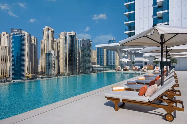 A rooftop pool with lounge chairs and umbrellas, overlooking a cityscape with high-rise buildings.