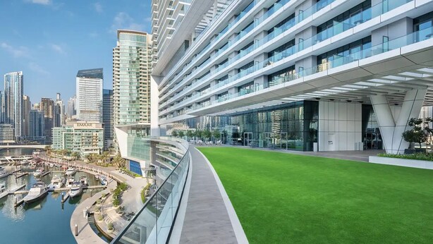 Un hôtel moderne doté d’une façade en verre incurvée, d’un jardin sur le toit et d’une marina avec des bateaux.