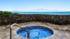 A hot tub with a stone wall and a view of the ocean.