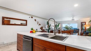 A modern kitchen with a white countertop, stainless steel sink, and wooden cabinets.