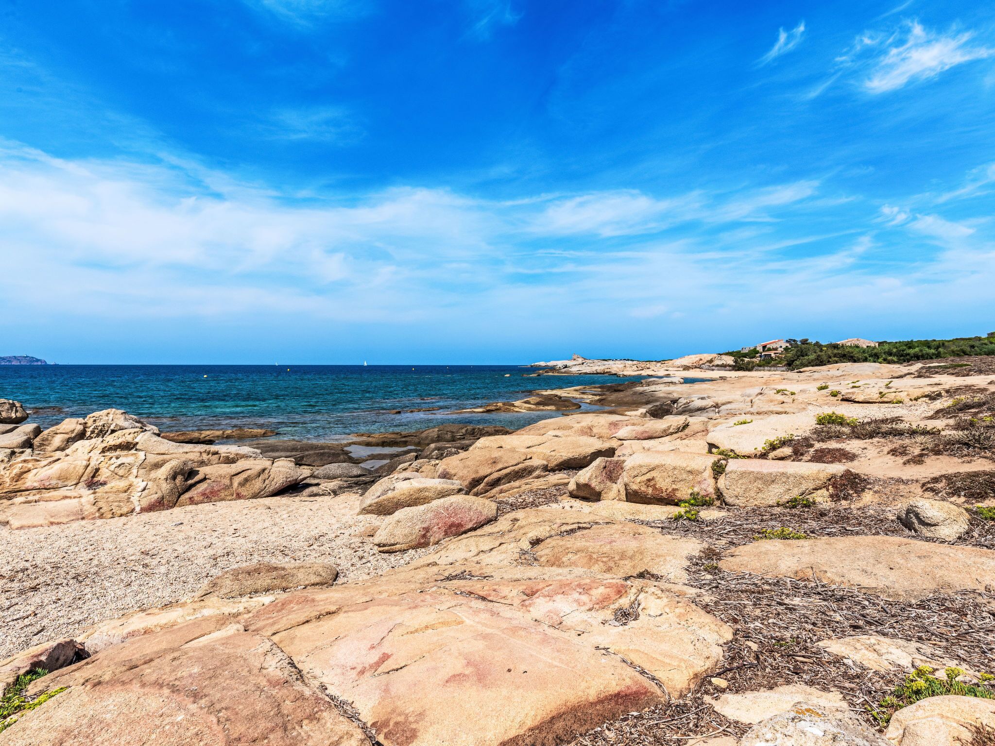 Platja rocosa amb mar blau clar i edificis a la distància.
