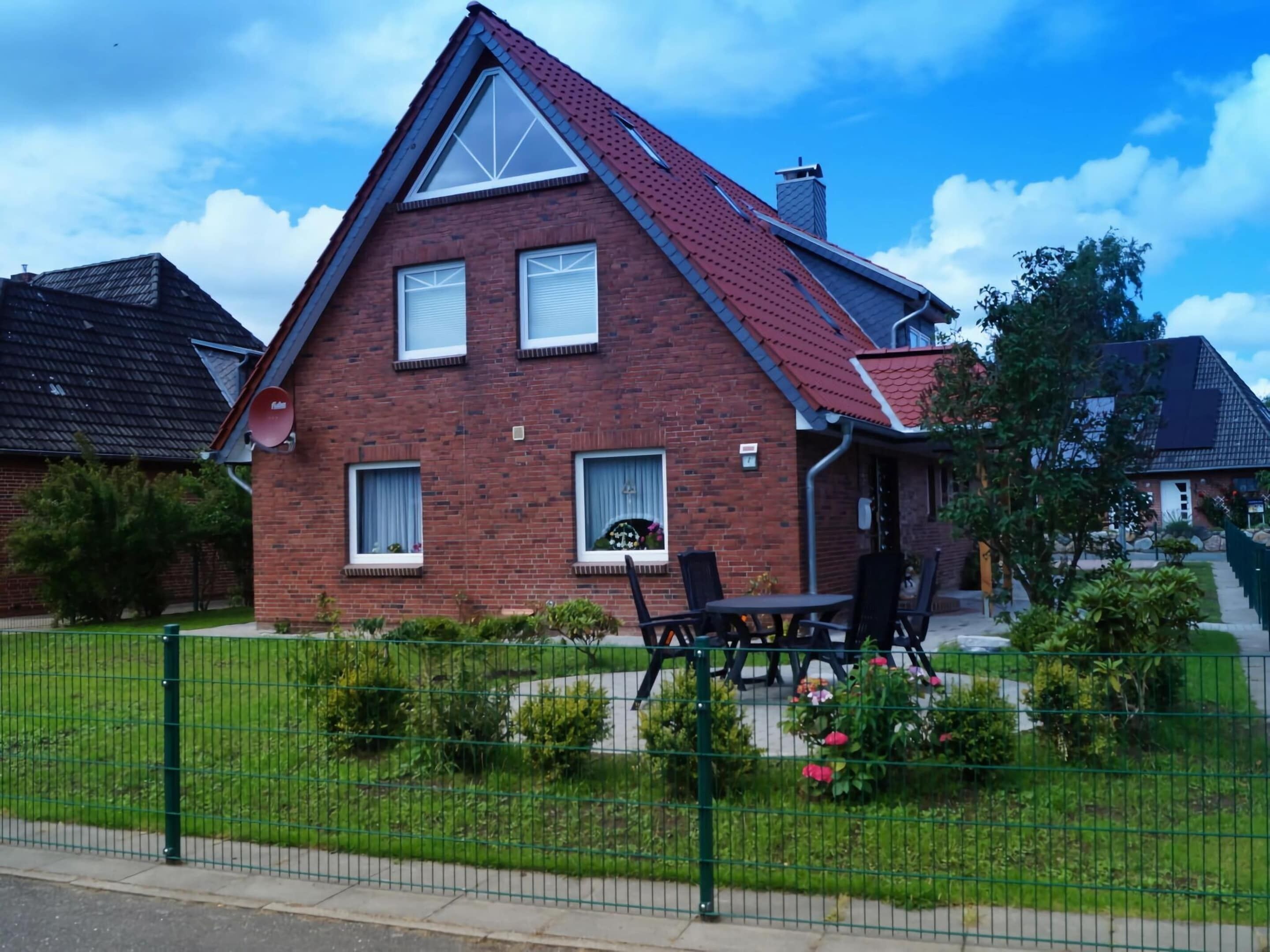 A two-story brick house with a red roof, a small front porch, and a green lawn.
