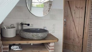 Een badkamer met een stenen wastafel, een spiegel en een houten deur.