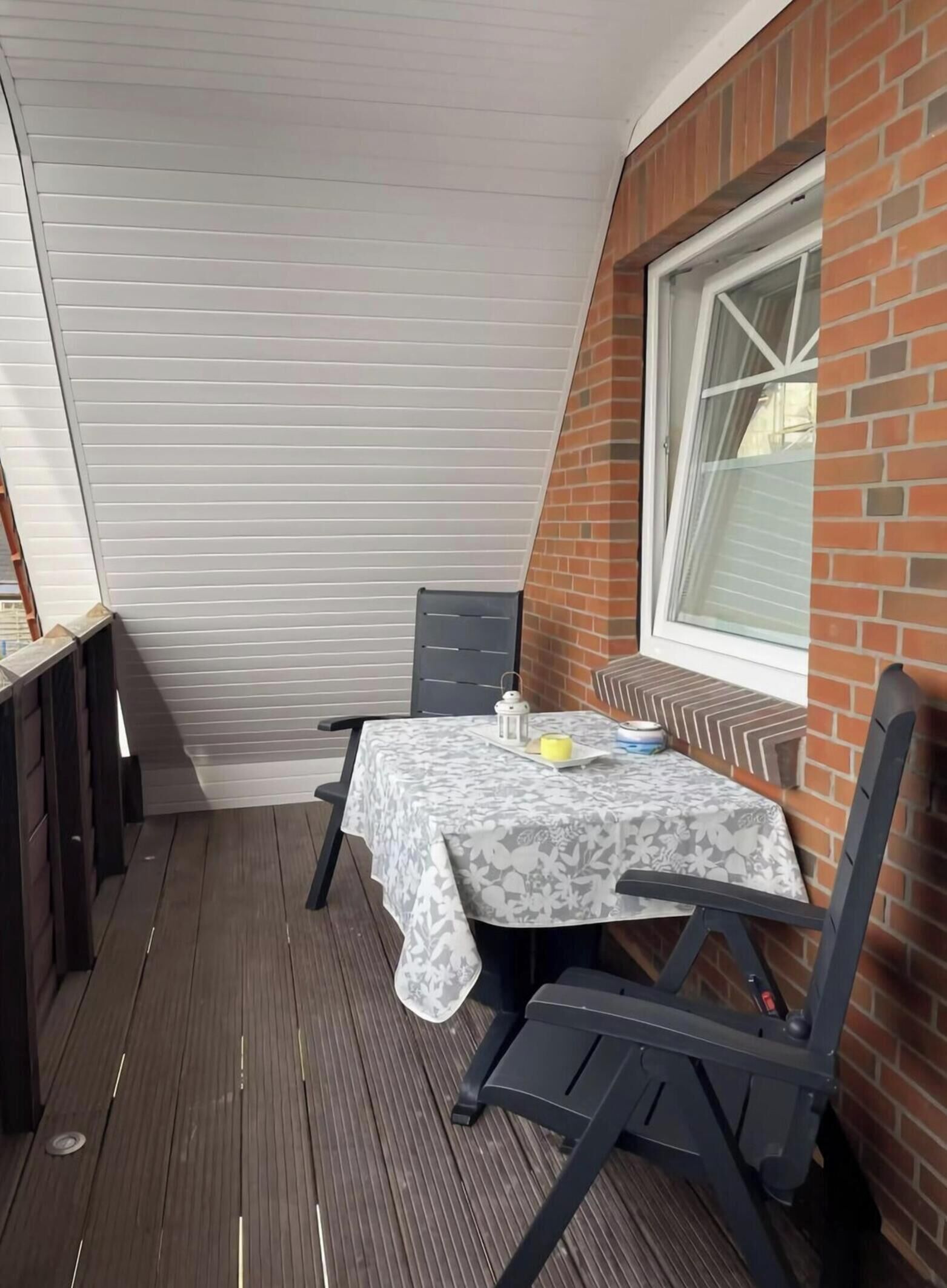 Ein kleiner Patio-Bereich mit Tisch und Stühlen, ein Fenster und eine Backsteinmauer.