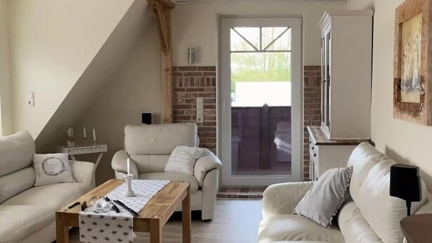Een ruime woonkamer met een hoge plafond, een houten salontafel, twee witte banken en een glazen schuifdeur naar een terras.