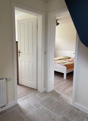 A room with a bed, a radiator, and a door leading to another room. - Holiday Apartment Eiderstedt (Toenning)