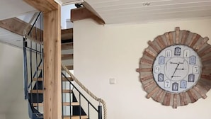 Een houten trap met zwarte leuningen die naar een verdieping leidt. Op de muur is een rustieke klok met cijfers en een datum bevestigd.