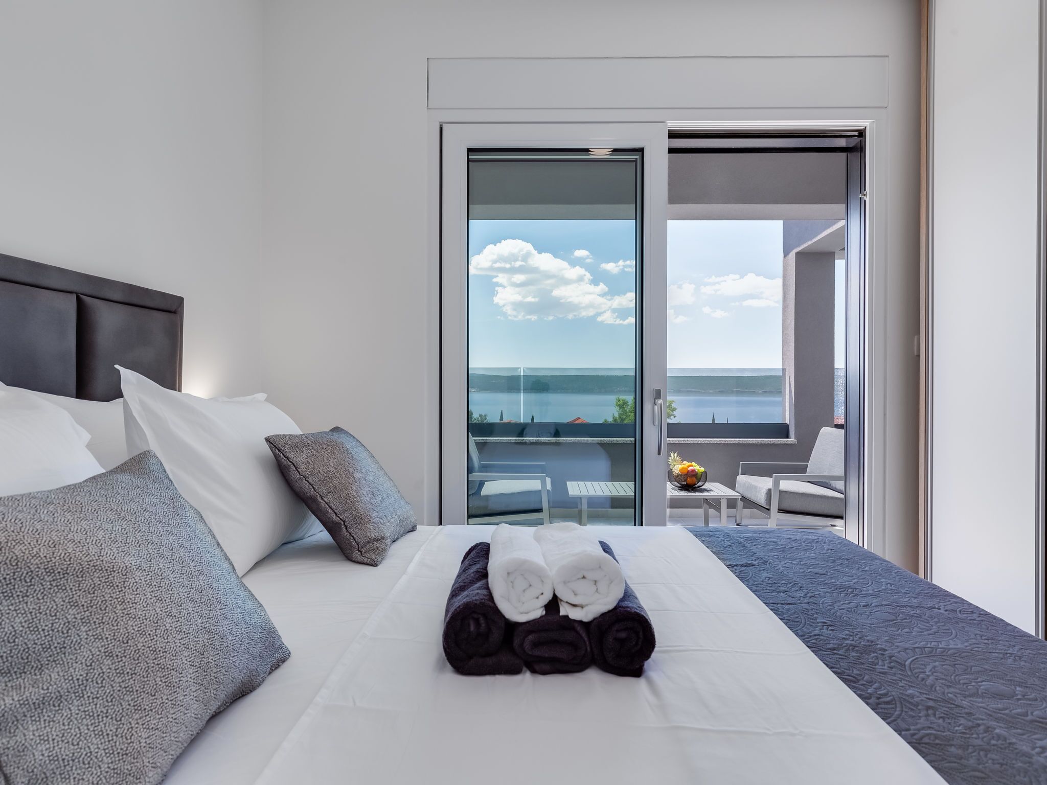 A hotel room with a bed, a view of the sea, and a balcony with a table and chairs.