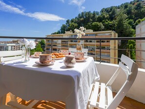A balcony with a table set for tea, surrounded by white chairs, overlooking a cityscape with buildings and trees. - L'Antonia by Interhome (Roquebrune Cap Martin)