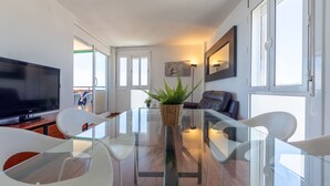 A modern living room with a glass dining table, white chairs, a flat-screen TV, a sofa, and a potted plant. - Apartment Garbi by Interhome (Cunit)