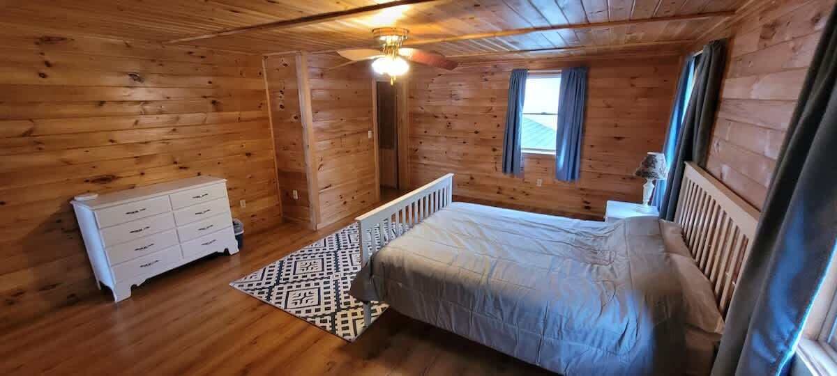 Een houten slaapkamer met een bed, een dressoir en een raam met gordijnen.