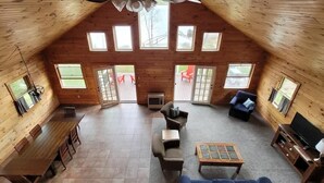 A spacious loft-style room with a high ceiling, large windows, a wooden floor, a sofa, a coffee table, and a TV. - Lakeside Luxury: Your Private Waterfront Escape (Lincoln)