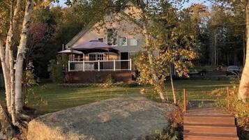 A wooden dock leading to a house with a porch, surrounded by trees and a small stream.