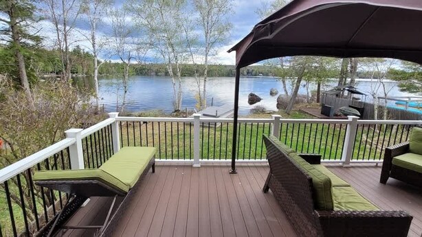 A deck with outdoor furniture, a view of a lake, and a covered area. - Lakeside Luxury: Your Private Waterfront Escape (Lincoln)