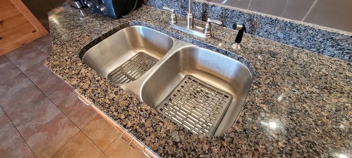 A kitchen with two stainless steel sinks, a granite countertop, and a tiled backsplash.