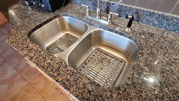 A kitchen with two stainless steel sinks, a granite countertop, and a tiled backsplash.