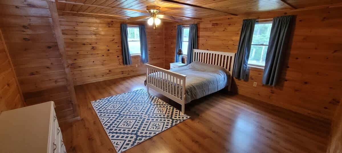 Camera da letto in una baita di legno, con un letto singolo, una culla bianca e un tappeto decorato.